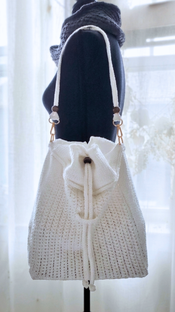 White textured knitted drawstring bucket bag on a mannequin - Orelia Purse Knitting Pattern| Purl Avenue